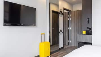 A hotel room with a bed, a television, a bathroom with a mirror, and a yellow suitcase.