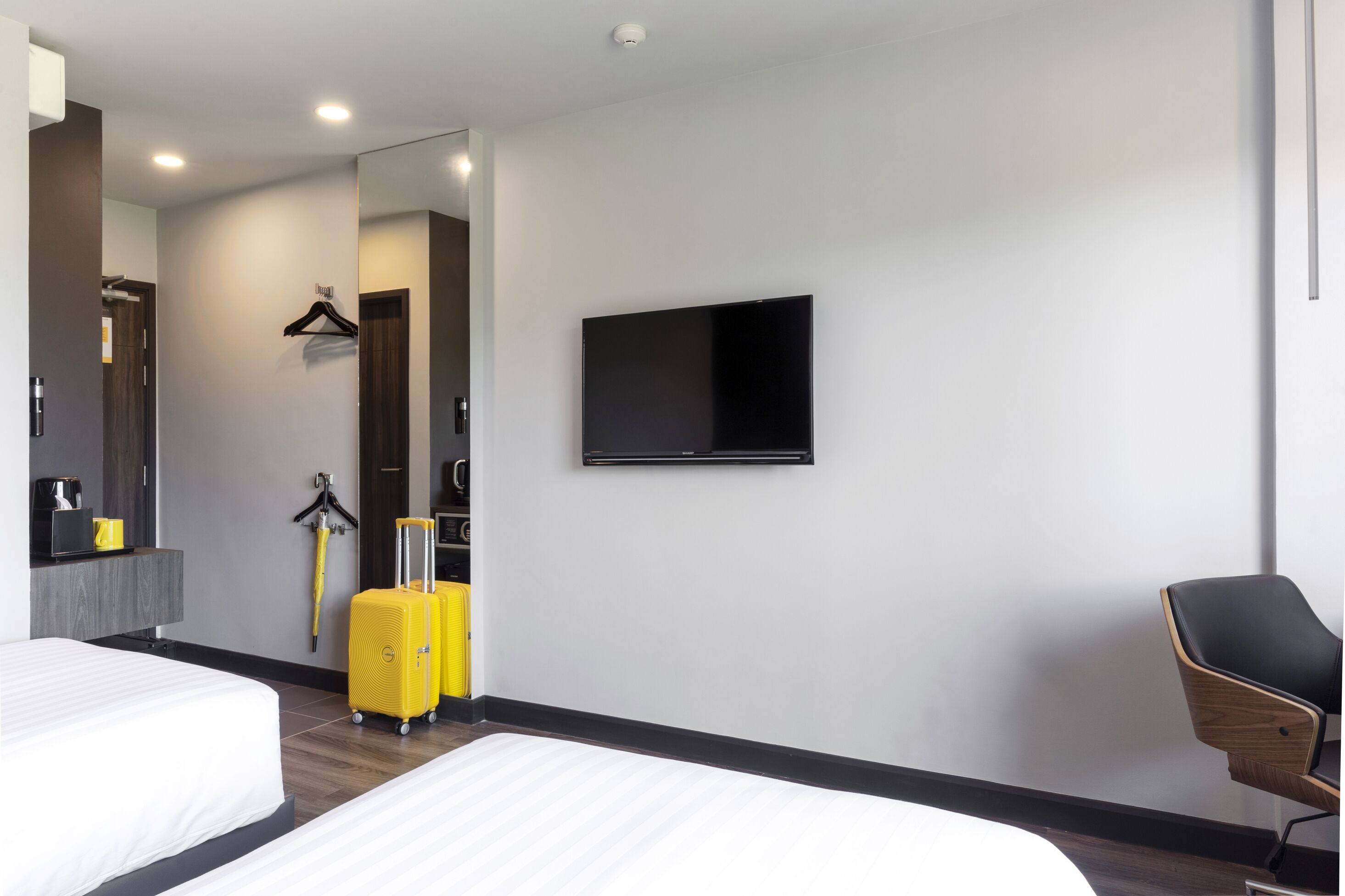 Ett hotellrum med två sängar, en platt-TV, en spegel, en klädställning och en resväska.