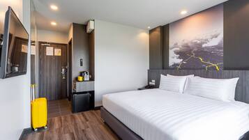Habitación de hotel con una cama grande, un espejo, un escritorio pequeño, una silla, una maleta y un televisor fijado a la pared.