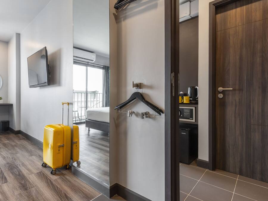 A hotel room with a bed, a desk, a chair, a TV, a coat rack, and a suitcase.