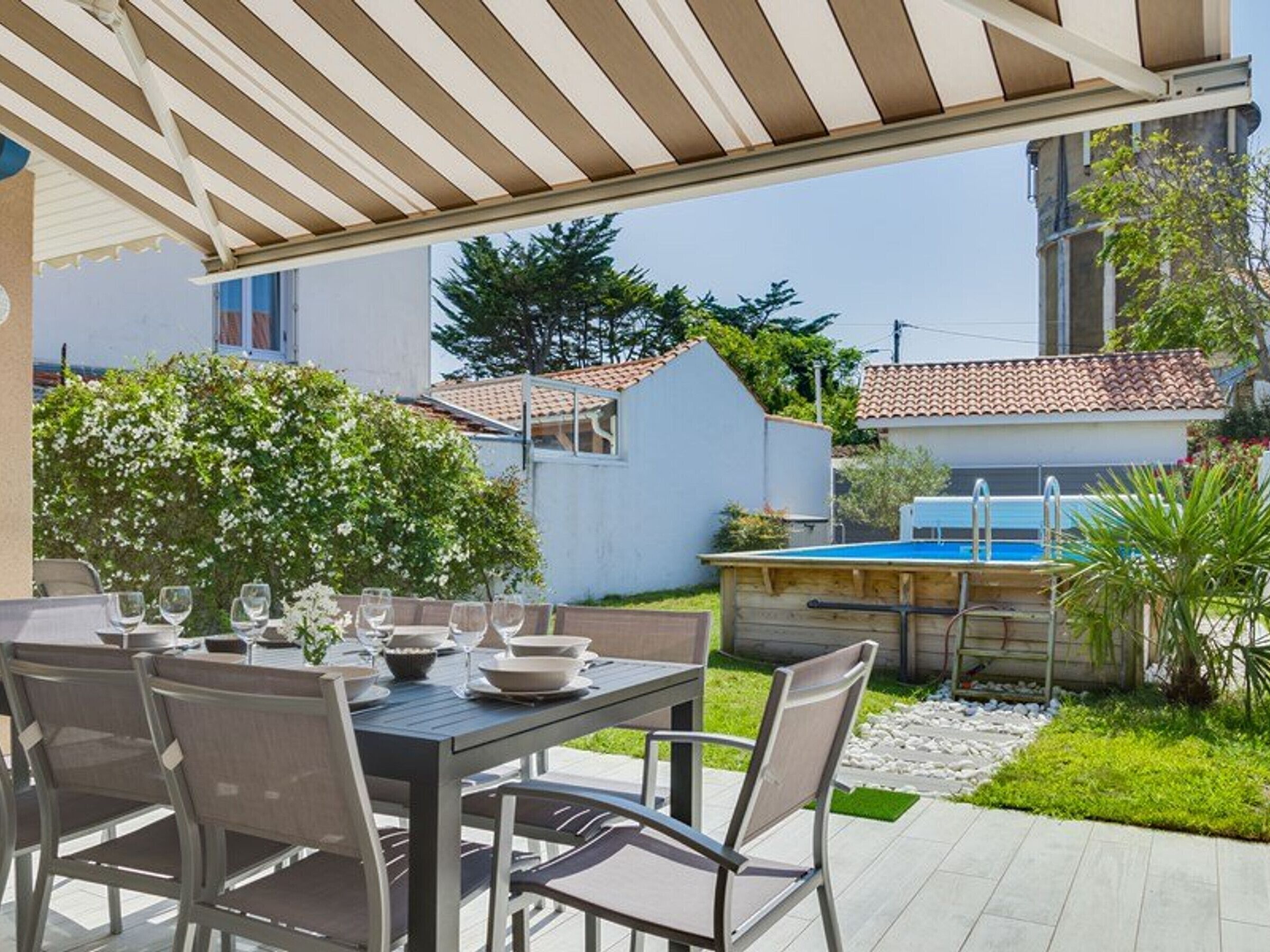 Un'area pranzo all'aperto con un tavolo apparecchiato per sei, circondato da sedie. Si intravede una piscina sullo sfondo.
