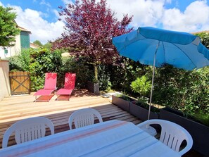 A wooden deck with a table and chairs, a blue umbrella, and red chairs.