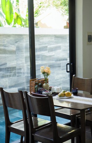 A dining area with a table set for two, featuring a vase with flowers, a basket, and a plate of fruit.