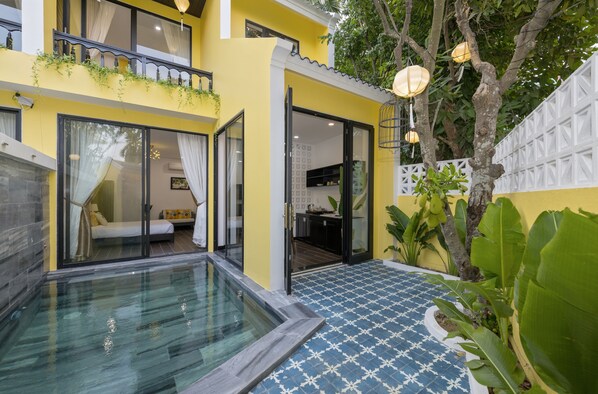 A modern building with a glass-enclosed swimming pool, a balcony with plants, and a tiled patio area.