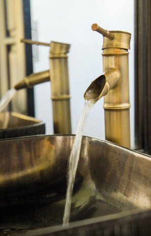 A brass water tap with water flowing into a metal basin.