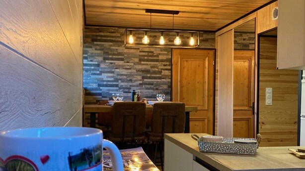 A cozy kitchen with wooden cabinets, a dining area with a table and chairs, and a coffee table with a magazine. - Cerdanya Family House (Font Romeu - Odeillo)