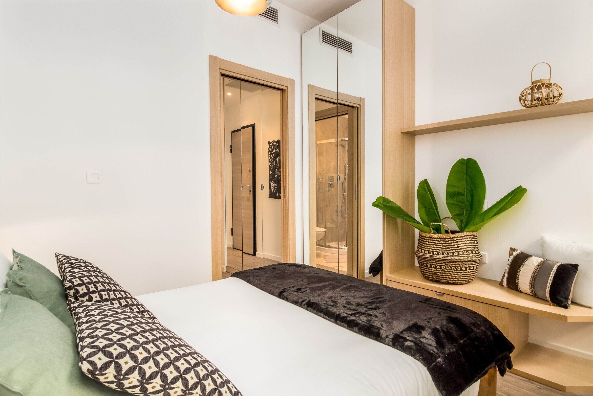 A modern bedroom with a bed, a bedside table, a plant, and a wardrobe.
