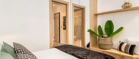 A modern bedroom with a bed, a bedside table, a plant, and a wardrobe.