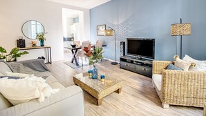 Een woonkamer met een bank, een rieten bijzettafeltje, een televisie en een lamp.