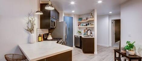 Una cocina moderna con una isla central, iluminación colgante y un comedor con una mesa pequeña y sillas.