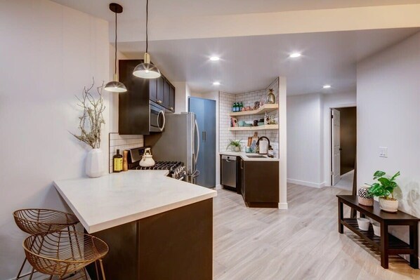 A modern kitchen with a central island, pendant lighting, and a dining area with a small table and chairs.