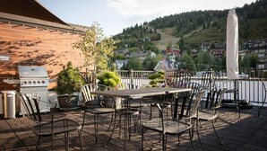 An outdoor patio with a brick wall, a grill, metal chairs, and a table. - The Sanctuary on Main Modern 1BR Walk to Town Lift (Park City)
