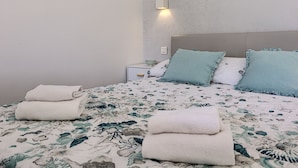 A neatly made bed with floral bedding, two pillows, and folded towels on a nightstand.