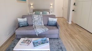 A modern bedroom with a grey sofa, a bedside table, and a nightstand.
