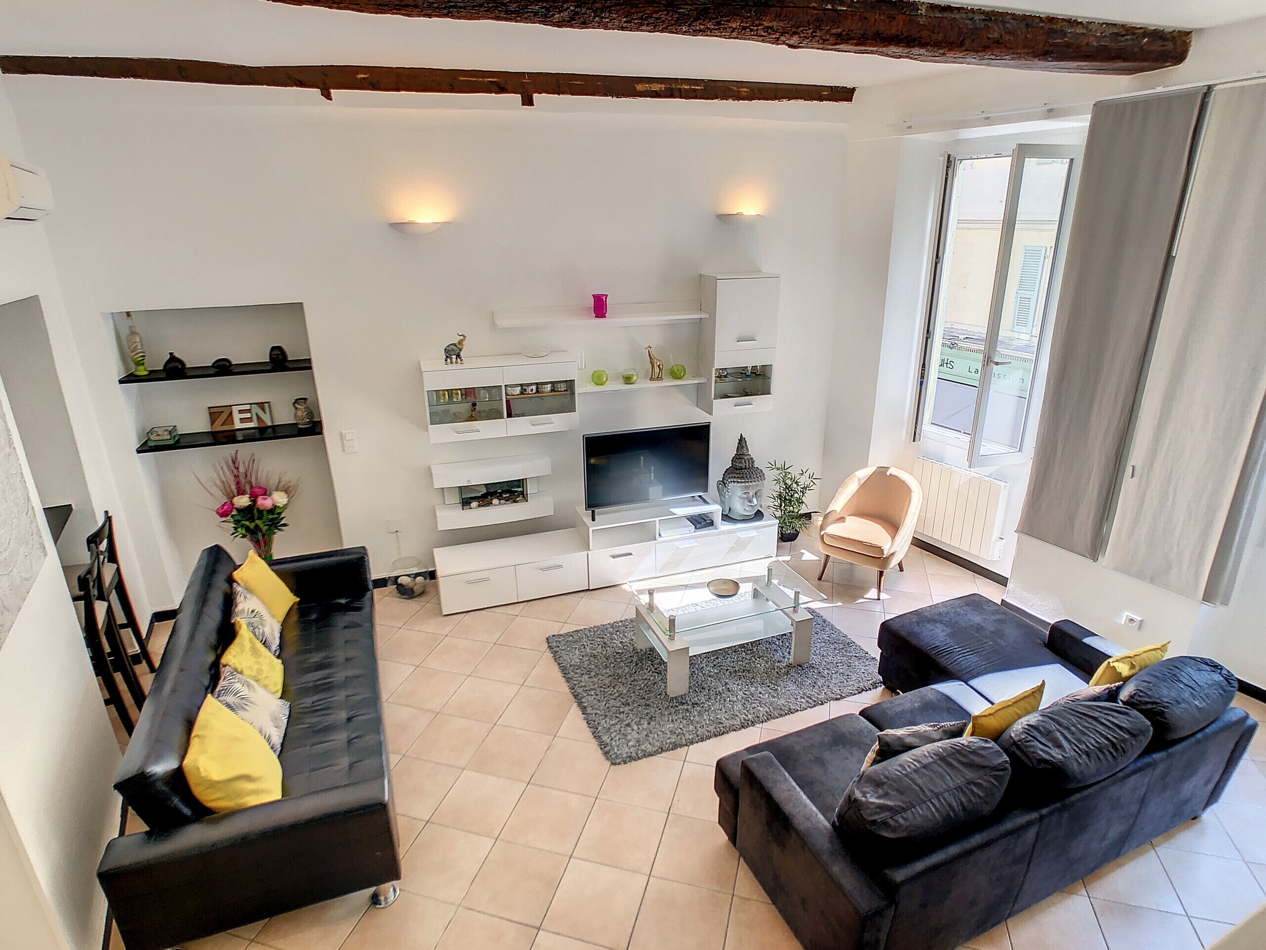 A modern living room with a black sofa, a black armchair, a glass coffee table, and a TV on a white entertainment unit.