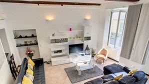A modern living room with a black sofa, a black armchair, a glass coffee table, and a TV on a white entertainment unit. - N&J - ZEN - Central - Very close sea - Spacious (Niza)