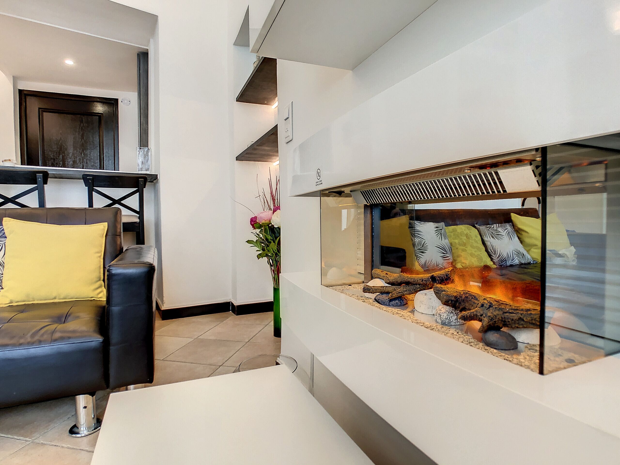 A modern interior with a seating area featuring a leather sofa and a glass enclosure with a fire feature.