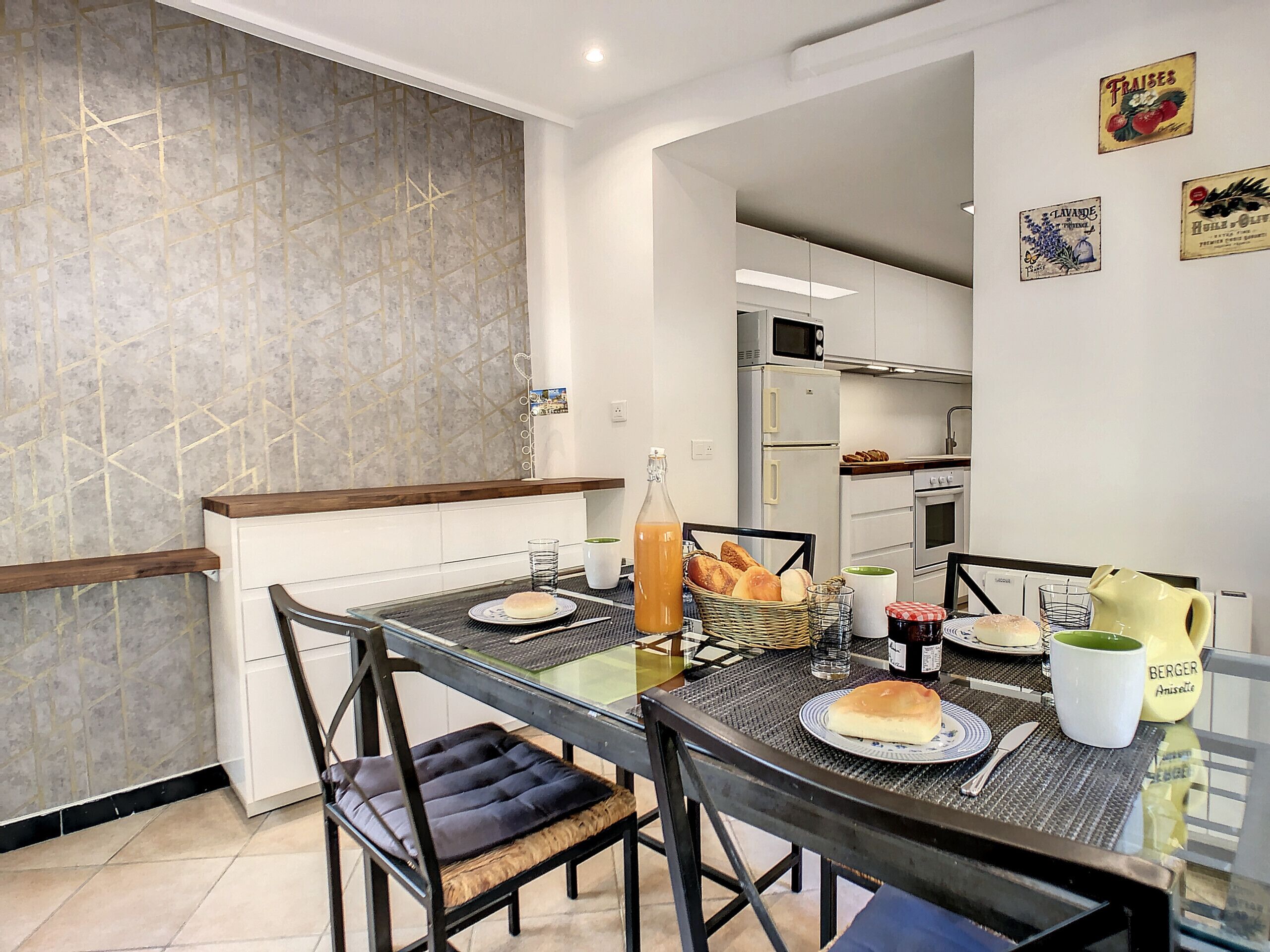 A dining area with a glass table, chairs, and a kitchen in the background.