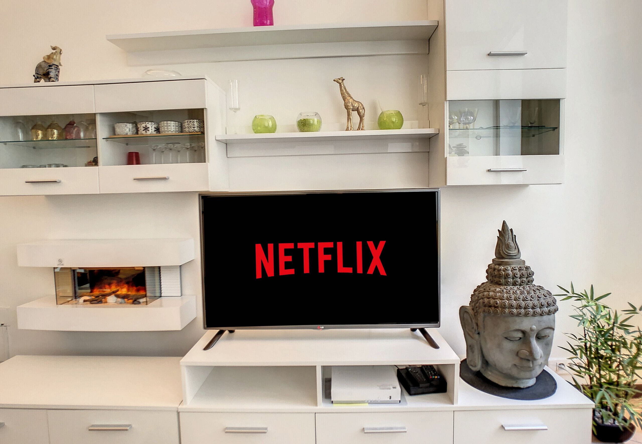 A modern living room with a flat-screen TV, white cabinets, decorative items, and a Buddha statue.