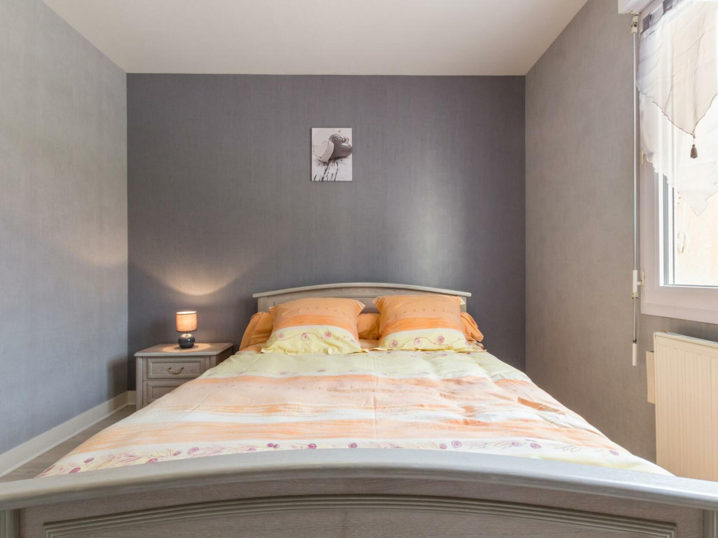 Une chambre à coucher avec un lit, une table de chevet, une lampe et un tableau accroché au mur.