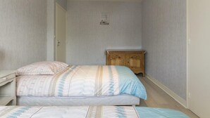 A bedroom with two beds, a wooden dresser, and a ceiling light.