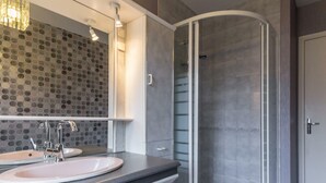 A modern bathroom with a curved shower enclosure, a double sink vanity, and a mosaic tile wall.