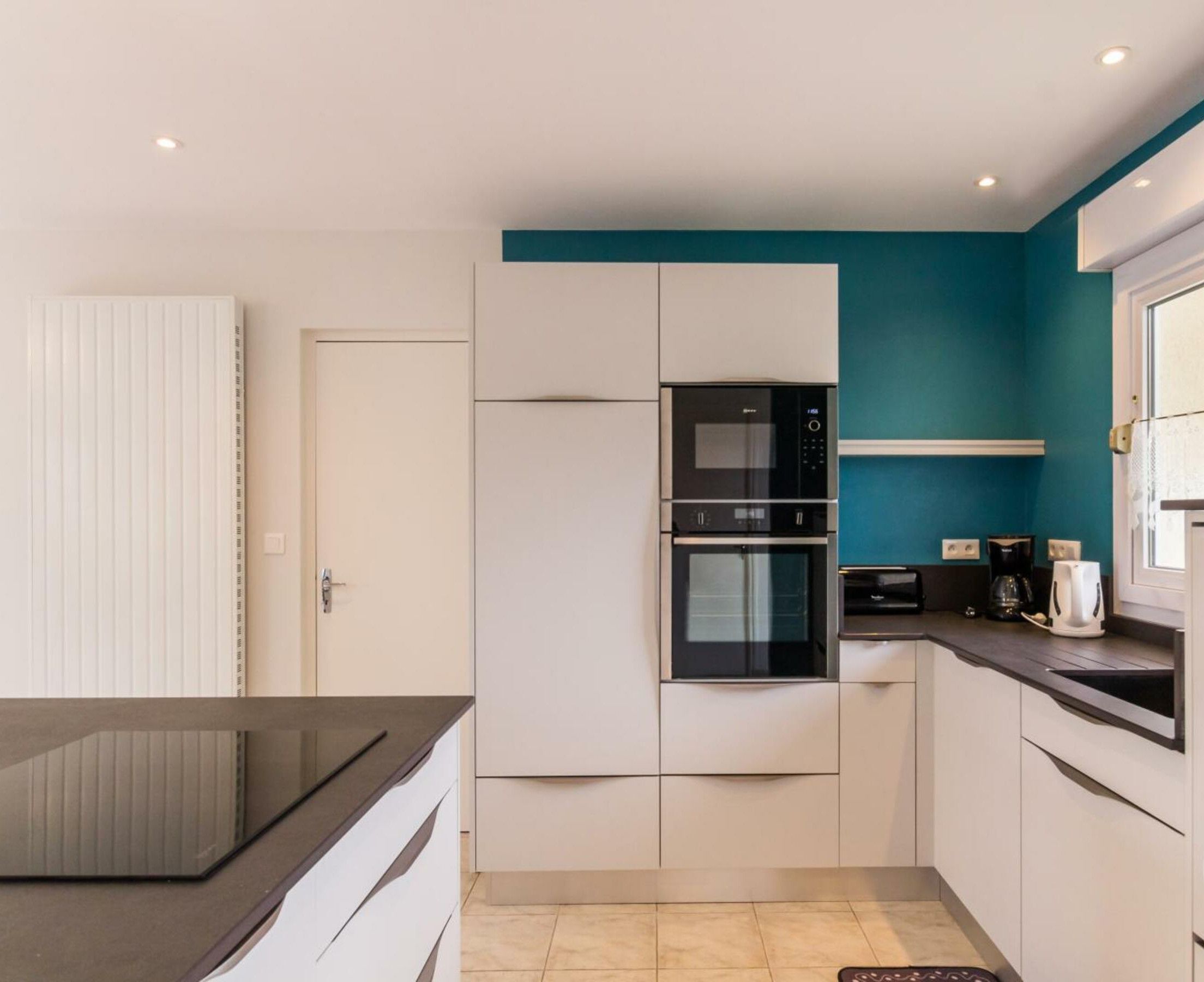 A modern kitchen with white cabinets, a black oven, and a teal accent wall.