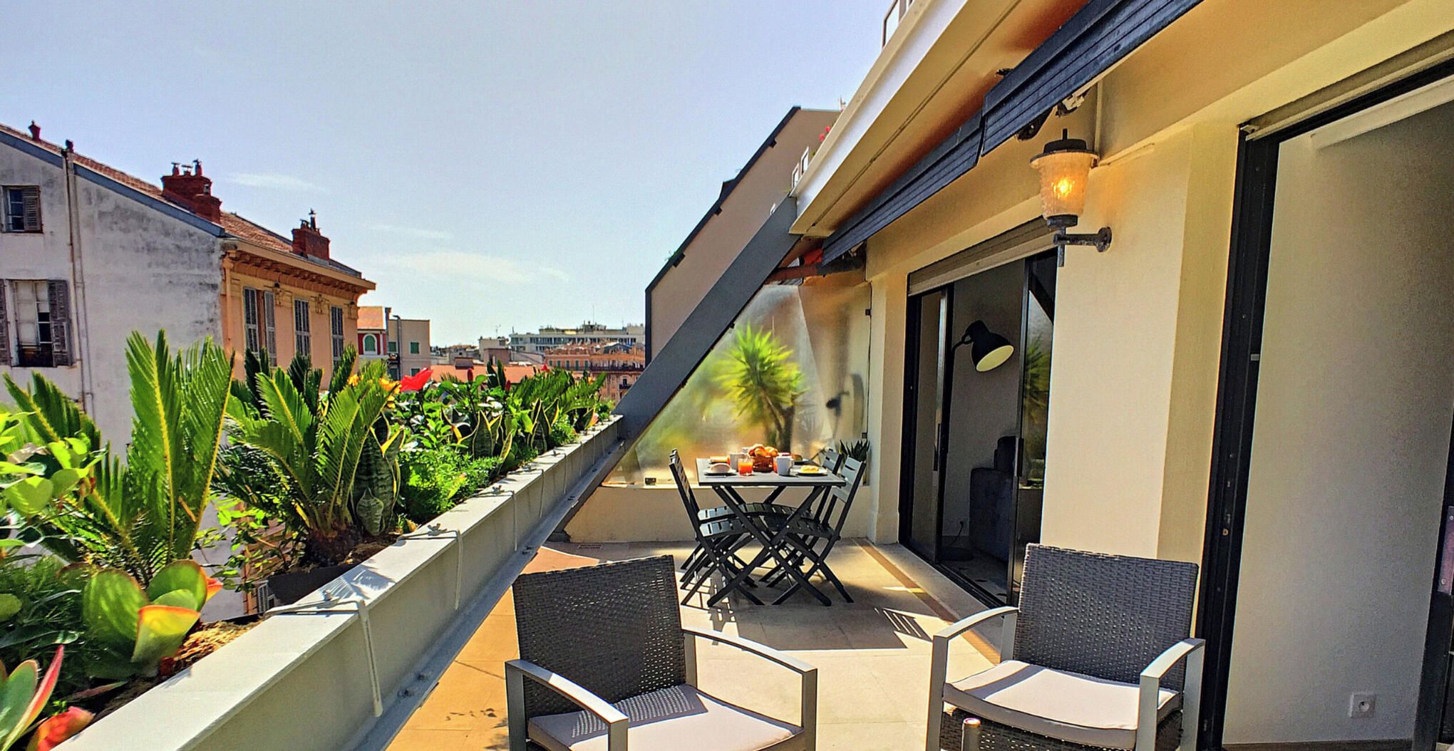 Terraza en la azotea con mesa y sillas, rodeada de plantas en macetas.