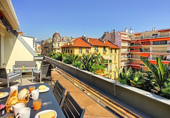 A rooftop terrace with a dining table set, outdoor furniture, and a view of surrounding buildings.