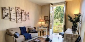 A living room with a sofa, a coffee table, and a dining area with chairs. There is a window with a view of greenery outside. - N&J - ANGEL'S BAY - Central - Close sea (Niza)