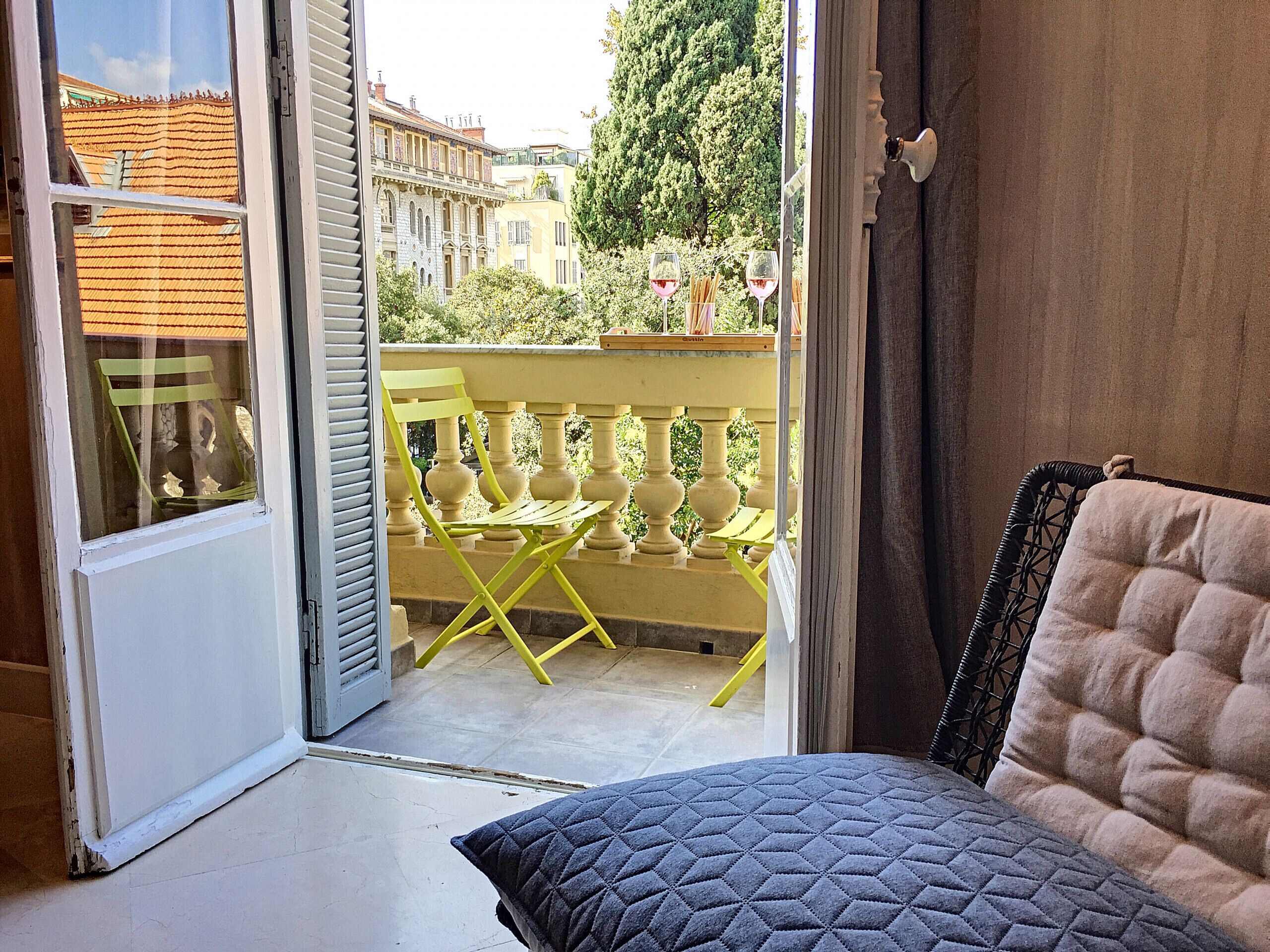 A balcony with yellow chairs and a table, a view of buildings, and a door leading outside.