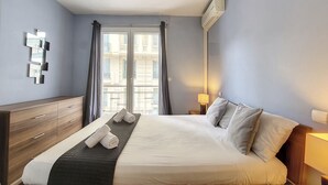 A hotel room with a bed, a wooden dresser, a wall-mounted air conditioning unit, and a window with curtains. - N&J - RIVIERA PROVENCE - CENTRAL - NEAR SEA (Niza)