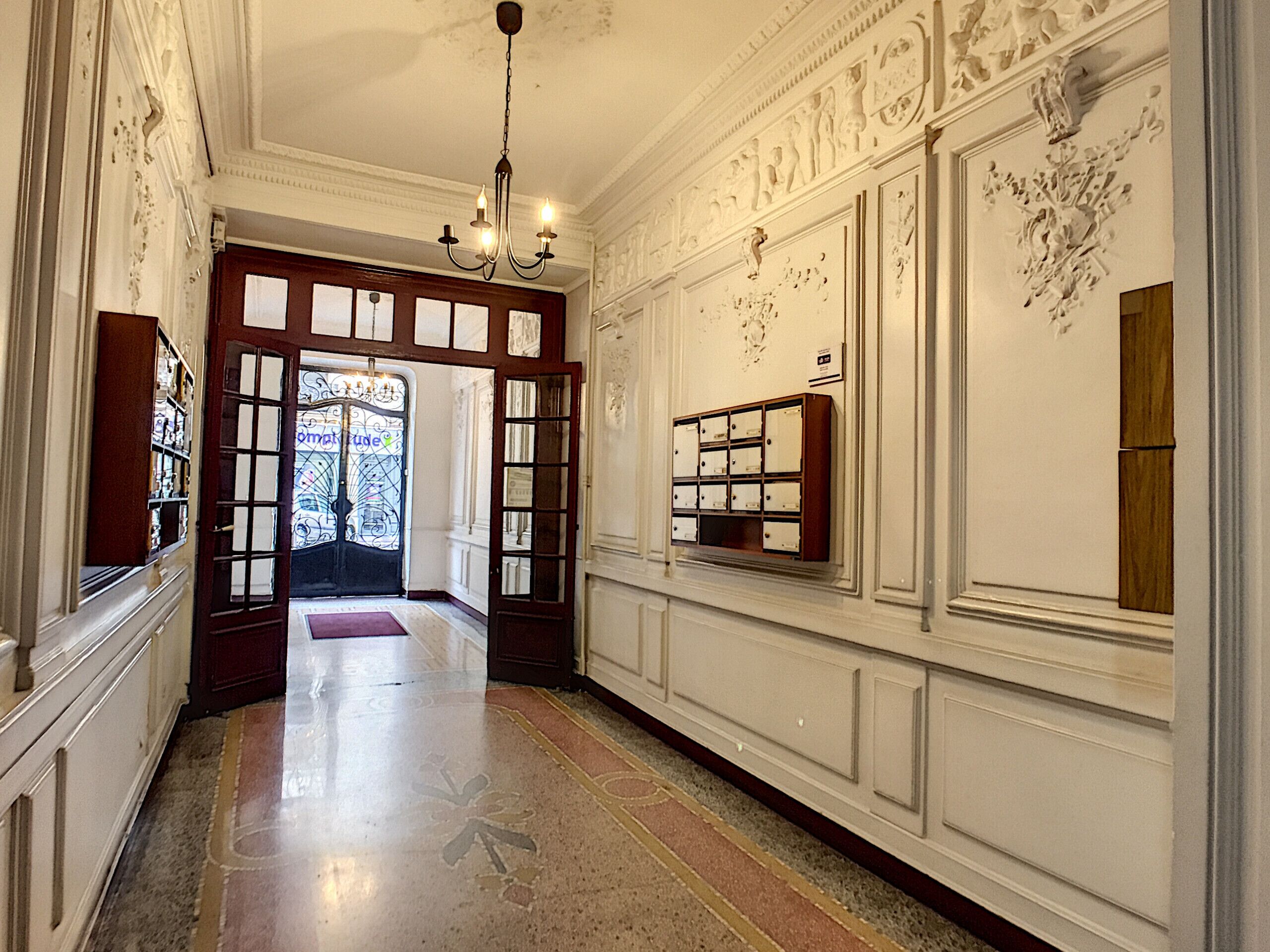 Un pasillo imponente con un candelabro, decoraciones ornamentales en las paredes y un aparador de madera con cajones.