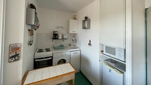 A compact kitchen with a stove, sink, and microwave. There is a small table and a washing machine.