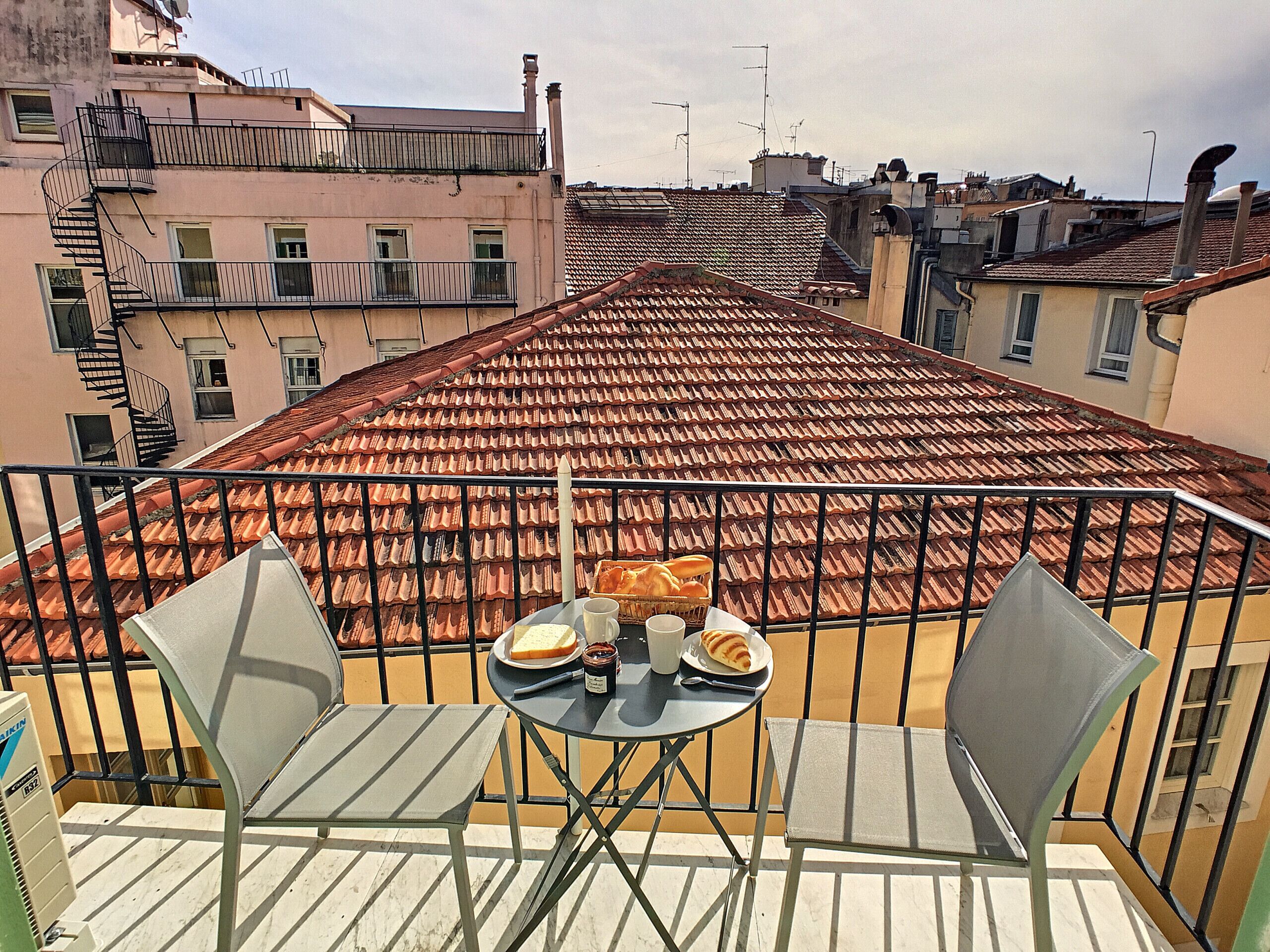 Een balkon met een tafel voor twee personen, met een broodmand en een fles water.