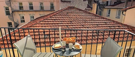 Een balkon met een tafel voor twee personen, met een broodmand en een fles water.