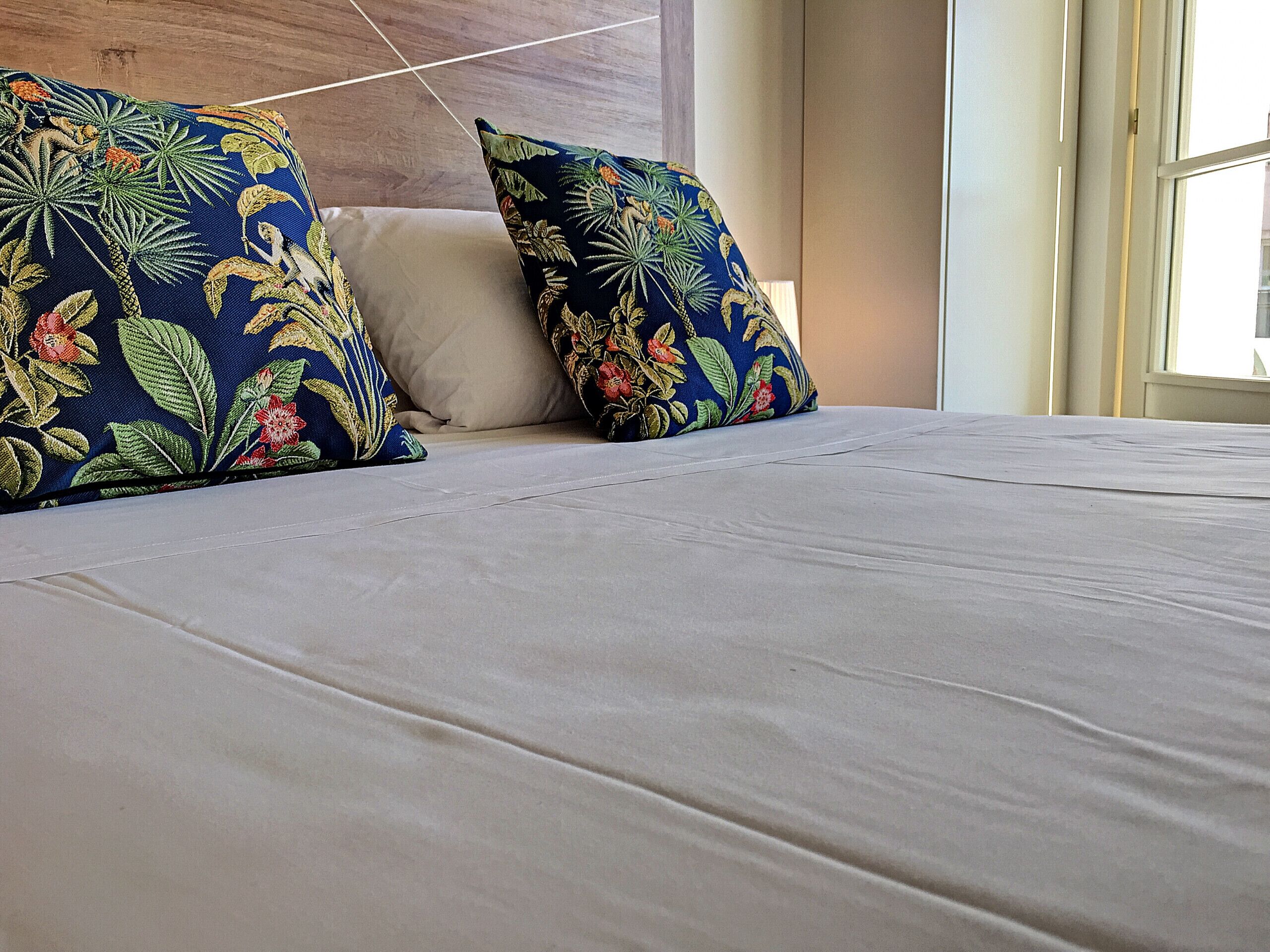 Cama bem arrumada com duas almofadas decorativas e um cobre-leito branco.