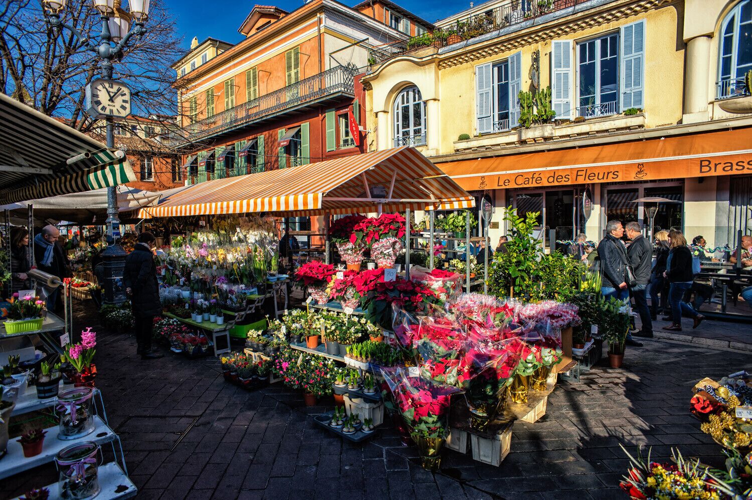 A flower market with various stalls and a café in the background.