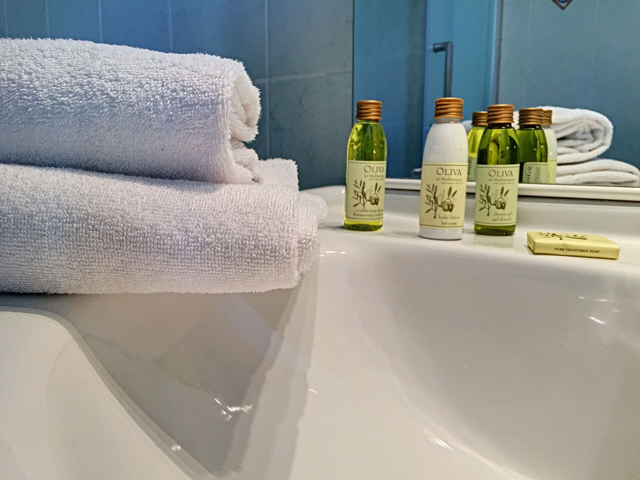 Ein Badezimmer mit einer weißen Badewanne, einem gefalteten weißen Handtuch und vier Flaschen auf Olivenöl basierenden Pflegeprodukten.