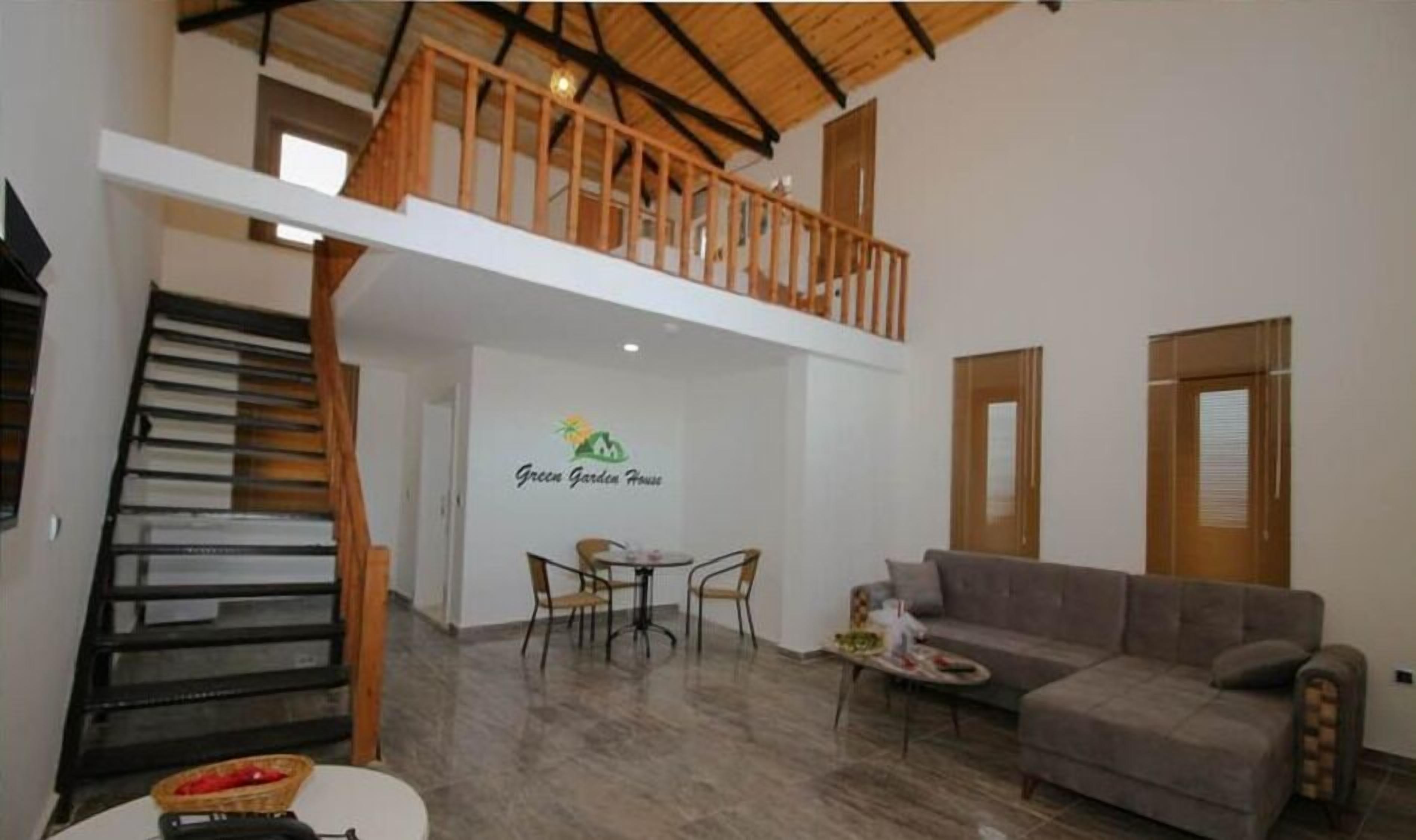 A spacious living area with a high ceiling, a staircase, a dining table with chairs, and a sofa.