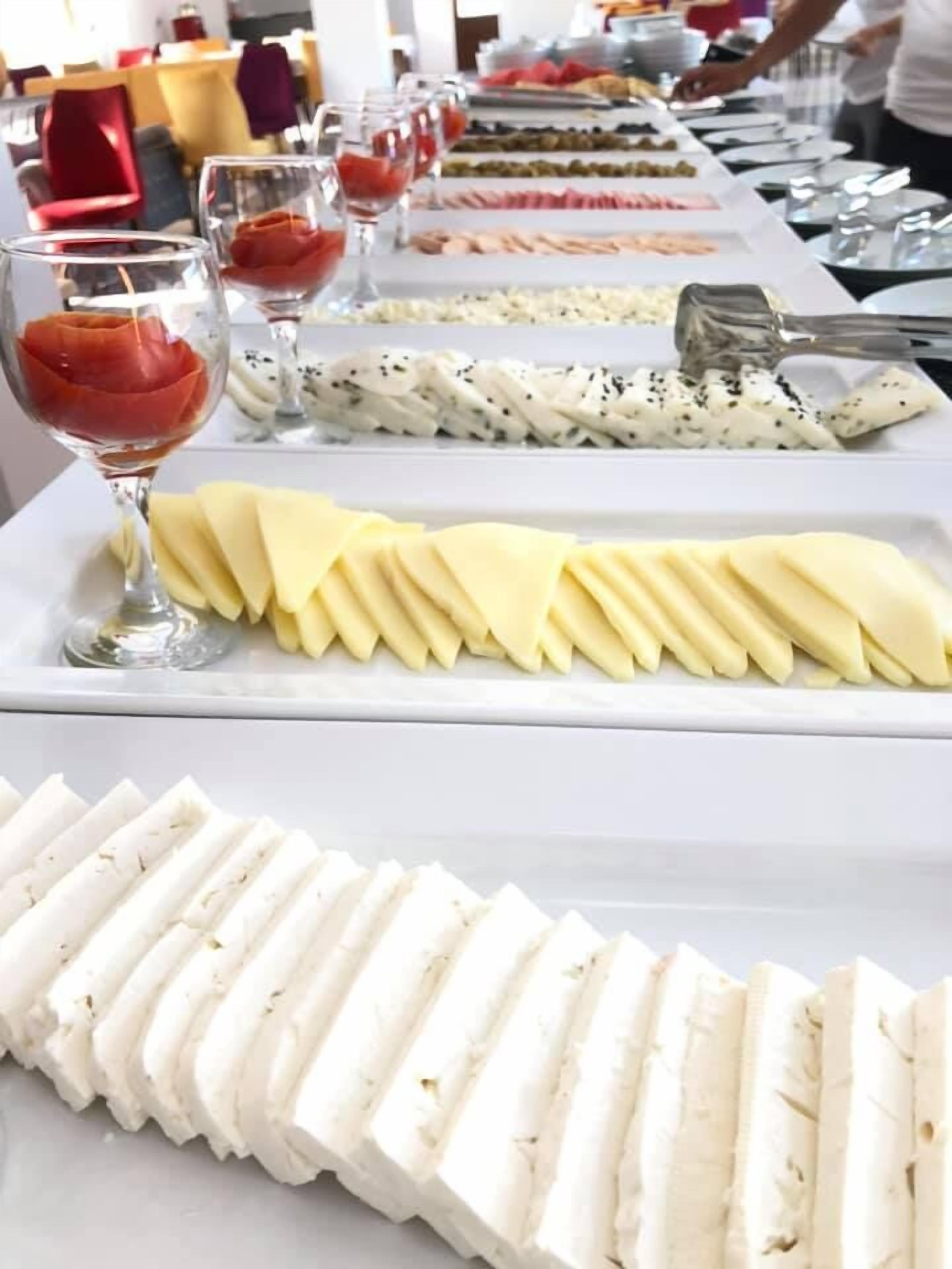 Una mesa de buffet con distintos alimentos, como queso en rodajas, frutas y una copa de vino tinto.