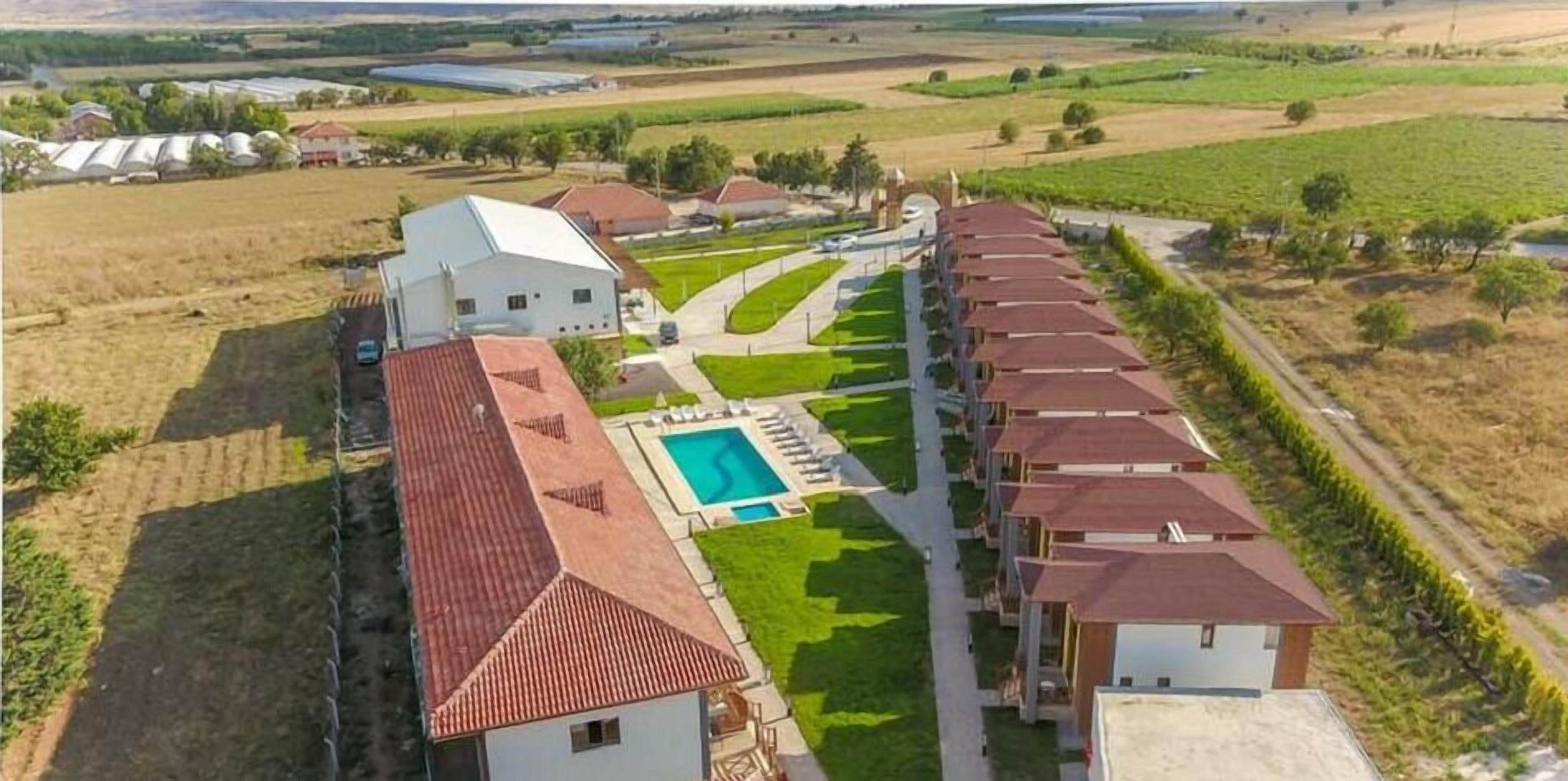 Zona residencial con piscina, un edificio blanco grande y una hilera de casas con tejados rojos.