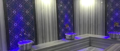 Zona de spa con una amplia bañera de piedra climatizada, dos lavamanos y una pared decorativa con un diseño geométrico.
