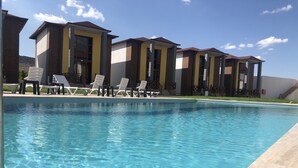 A swimming pool with clear water, surrounded by lounge chairs and a row of buildings with a modern architectural style. - Green Garden House Hotel&Spa (Tefenni)