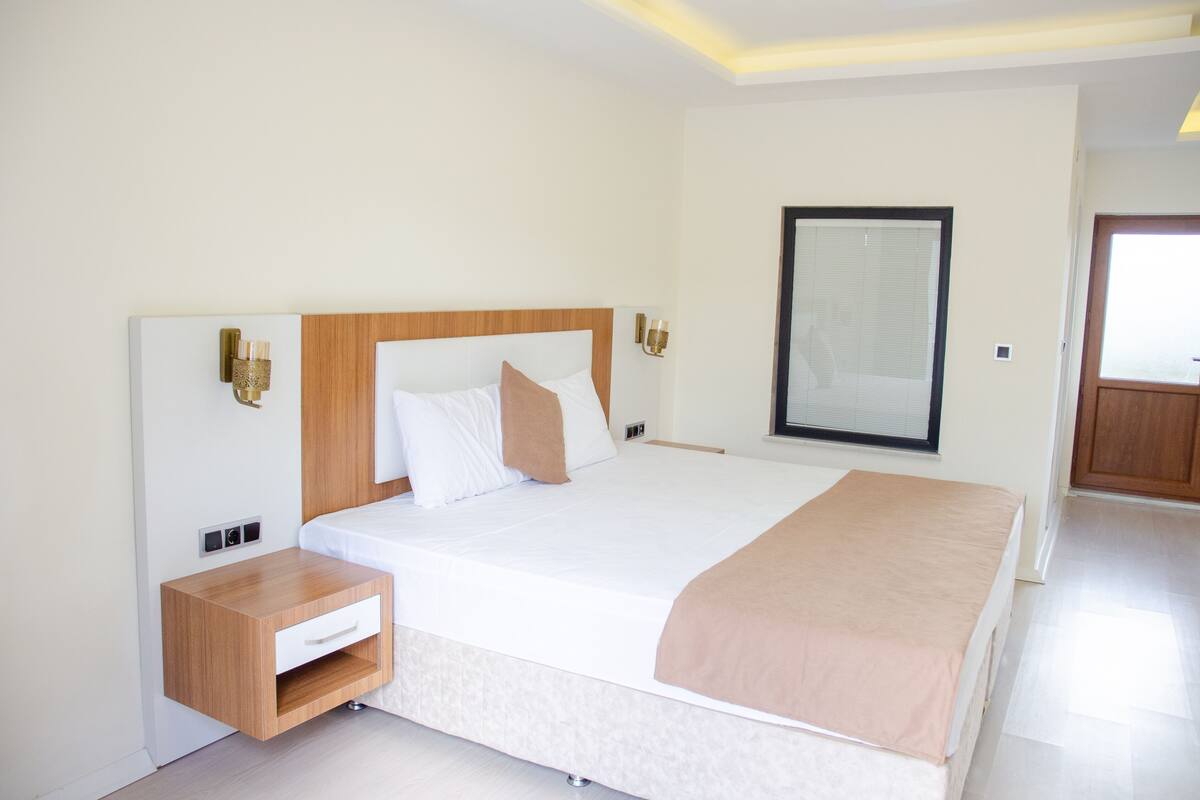 Moderni hotellihuone, jossa on suuri sänky, puinen yöpöytä, sängyn vieressä oleva pöytä ja peili seinällä.
