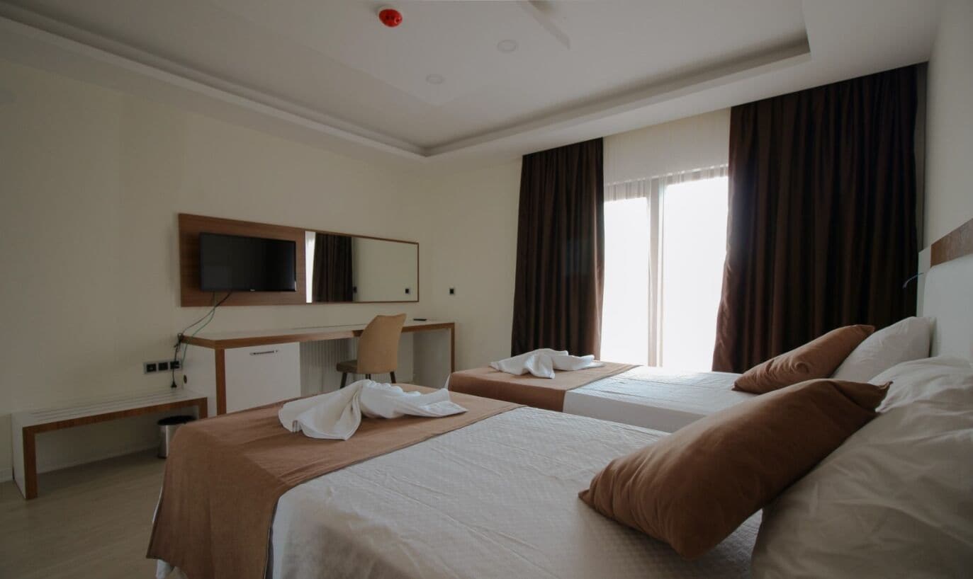 A hotel room with two beds, a desk, a chair, a TV, and a window with curtains.