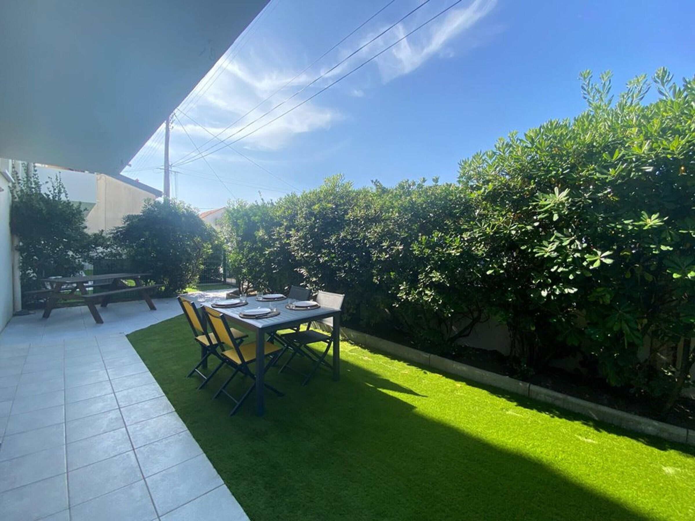 A patio with a table and chairs, surrounded by a well-maintained lawn and dense shrubbery.
