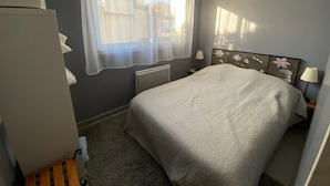A bedroom with a bed, a radiator, a window with sheer curtains, and a nightstand with a lamp. - Garden-Level Apartment 100m from Beach with Parking & Terrace (Capbreton)