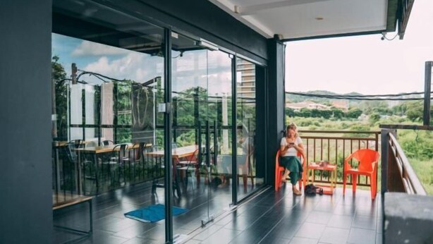 A balcony with a glass door leading to a dining area, a view of the countryside, and a person standing by the door. - Bed Attitude Hostel Cenang (Langkawi)