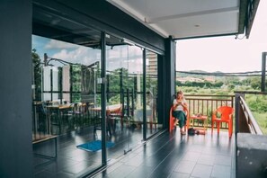 A balcony with a glass door leading to a dining area, a view of the countryside, and a person standing by the door. - Bed Attitude Hostel Cenang (Langkawi)